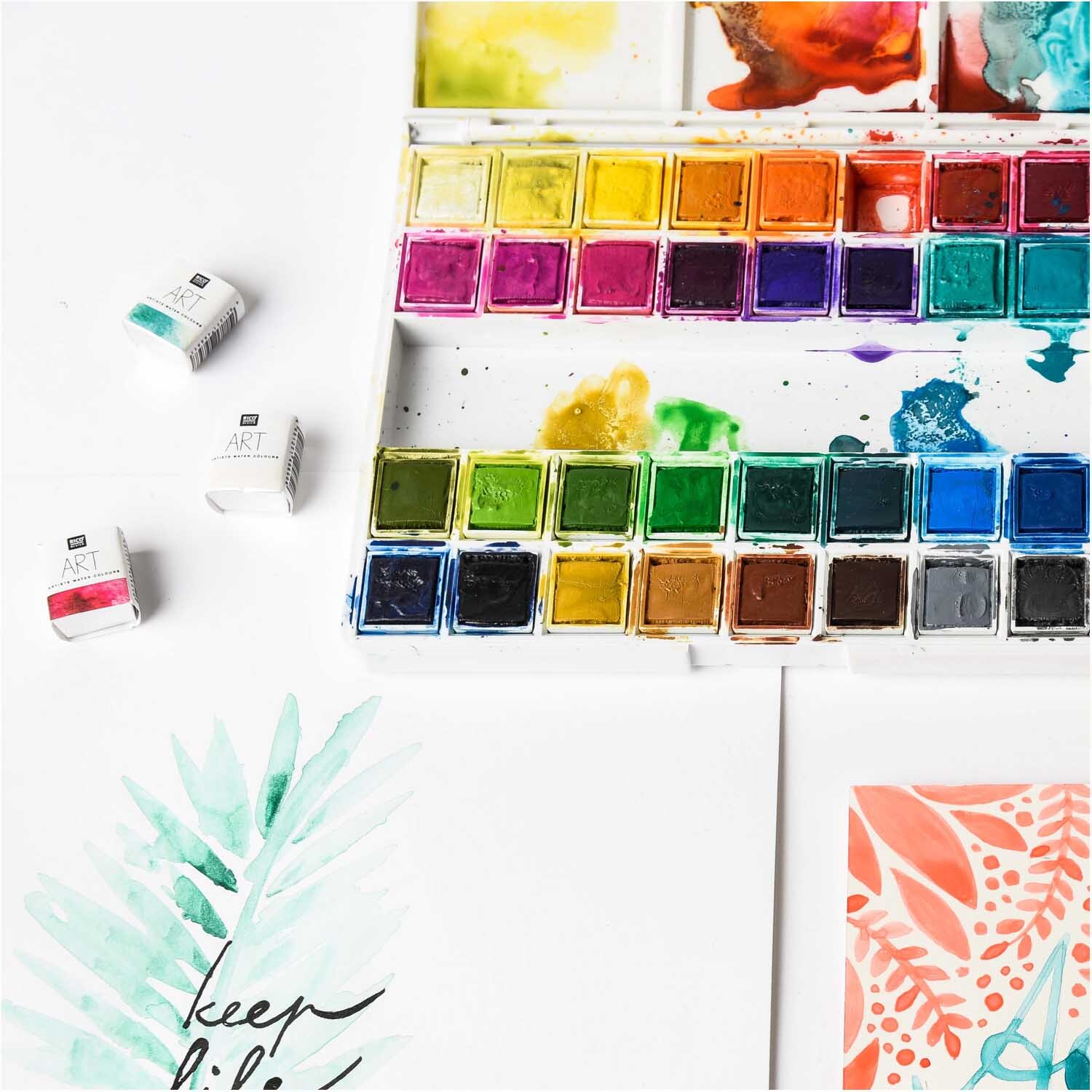 ART Künstler Aquarellfarben 36 Farben von Rico Design, präsentiert in einer Palette mit lebendigen Farbtönen und kreativen Kunstwerken im Hintergrund.