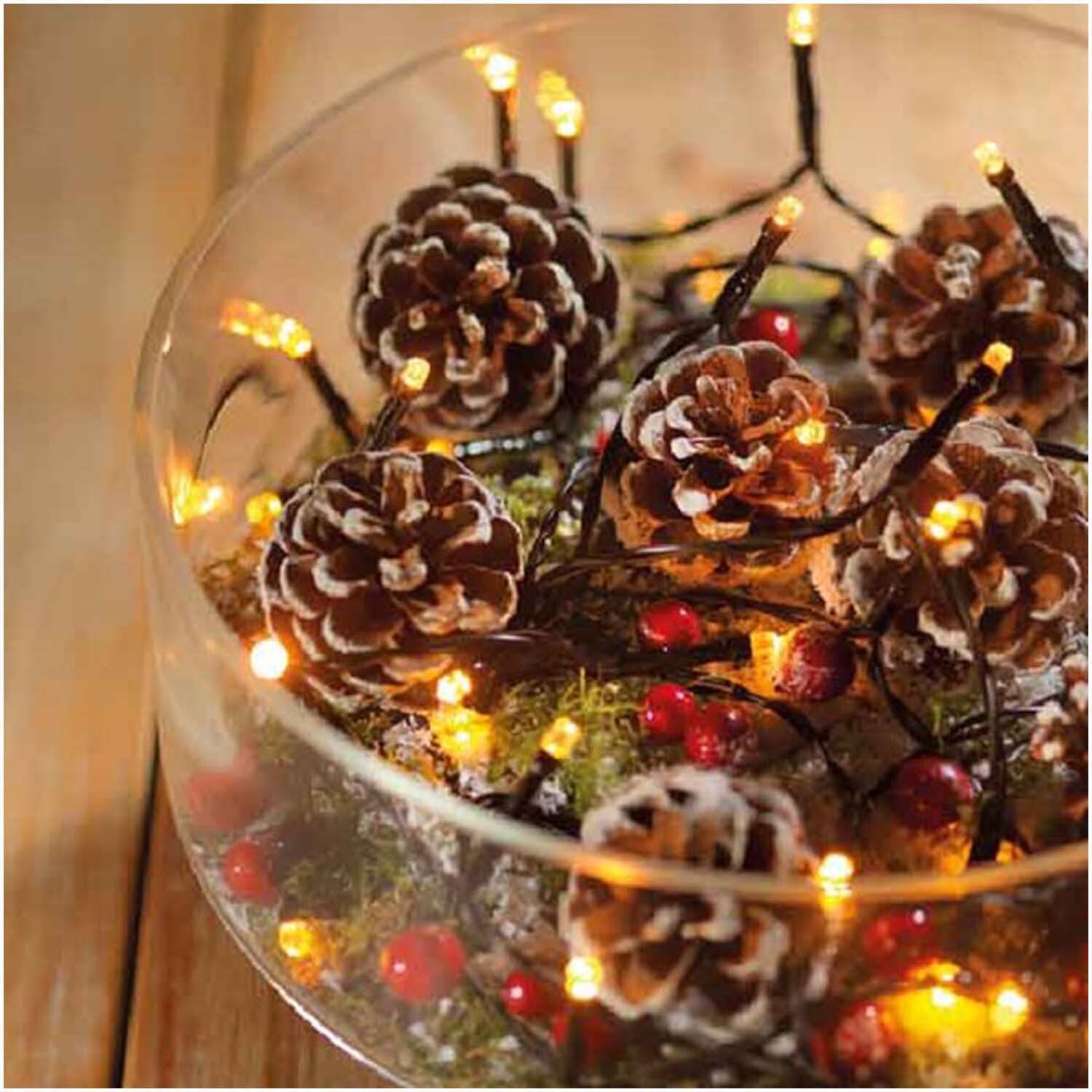 LED-Kette Durawise Basic beleuchtet Tannenzapfen und Beeren in einer Glasschale festlich.