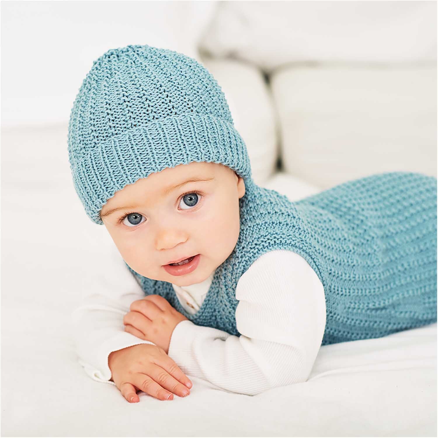 Rico Baby Cotton Soft dk: Baby in gestricktem Set aus weicher Wolle, liegend auf weißem Hintergrund.