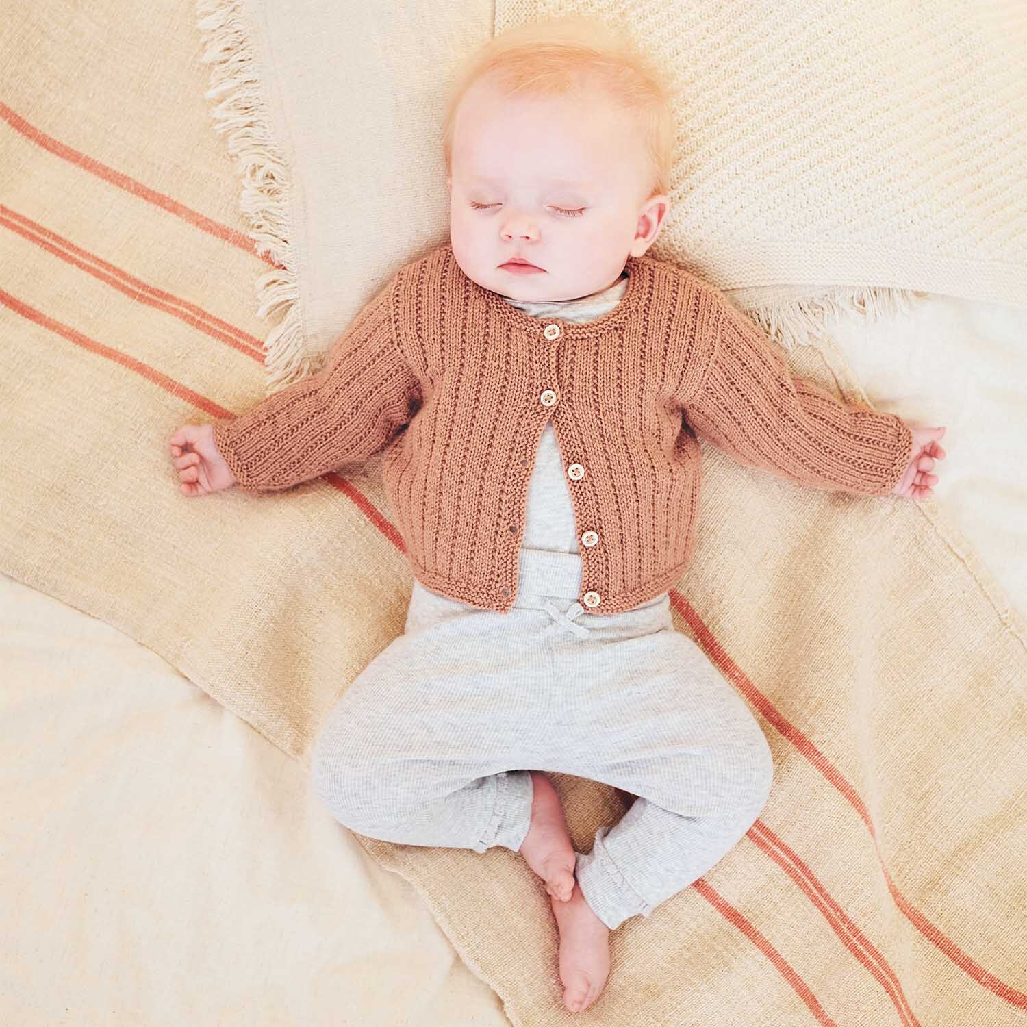 Strickanleitung Jacke aus Baby Merino: Ein Baby schläft in einer gestrickten Jacke auf einer Decke.
