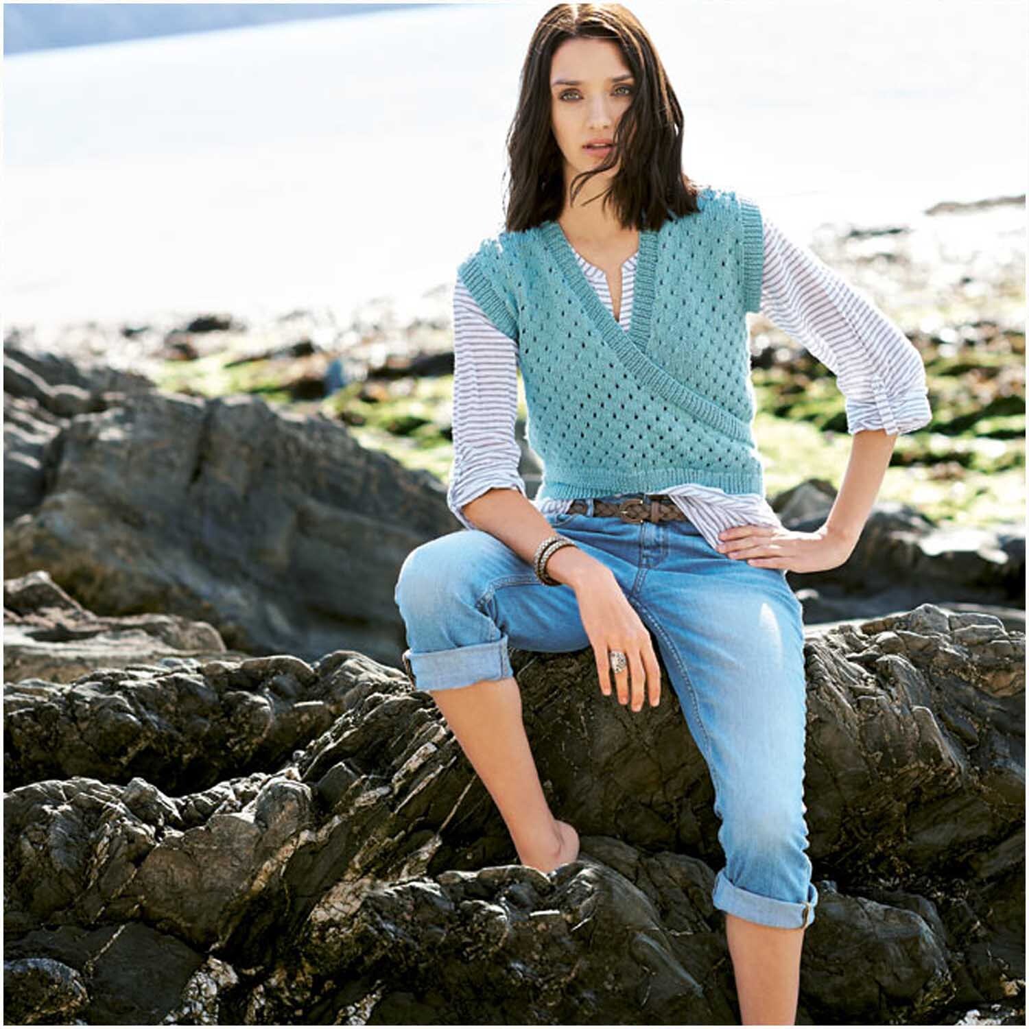 Creative Silky Touch dk: Frau in gestricktem Aqua-Top von Rico Design, sitzt auf Felsen am Strand.