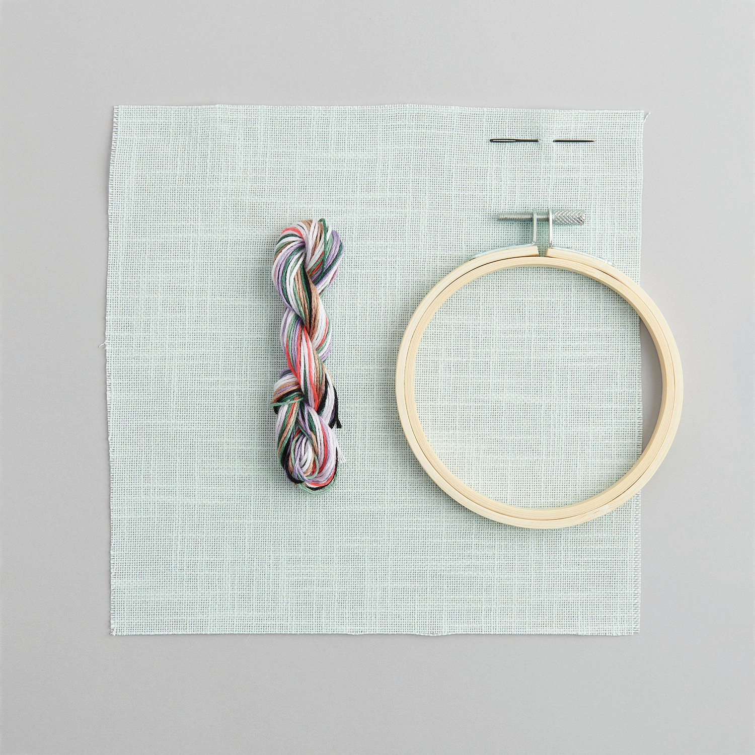 Stickpackung Bild Hase mit Gans im Arm: Stickrahmen, Garn und Stoff von Rico Design auf grauem Hintergrund.