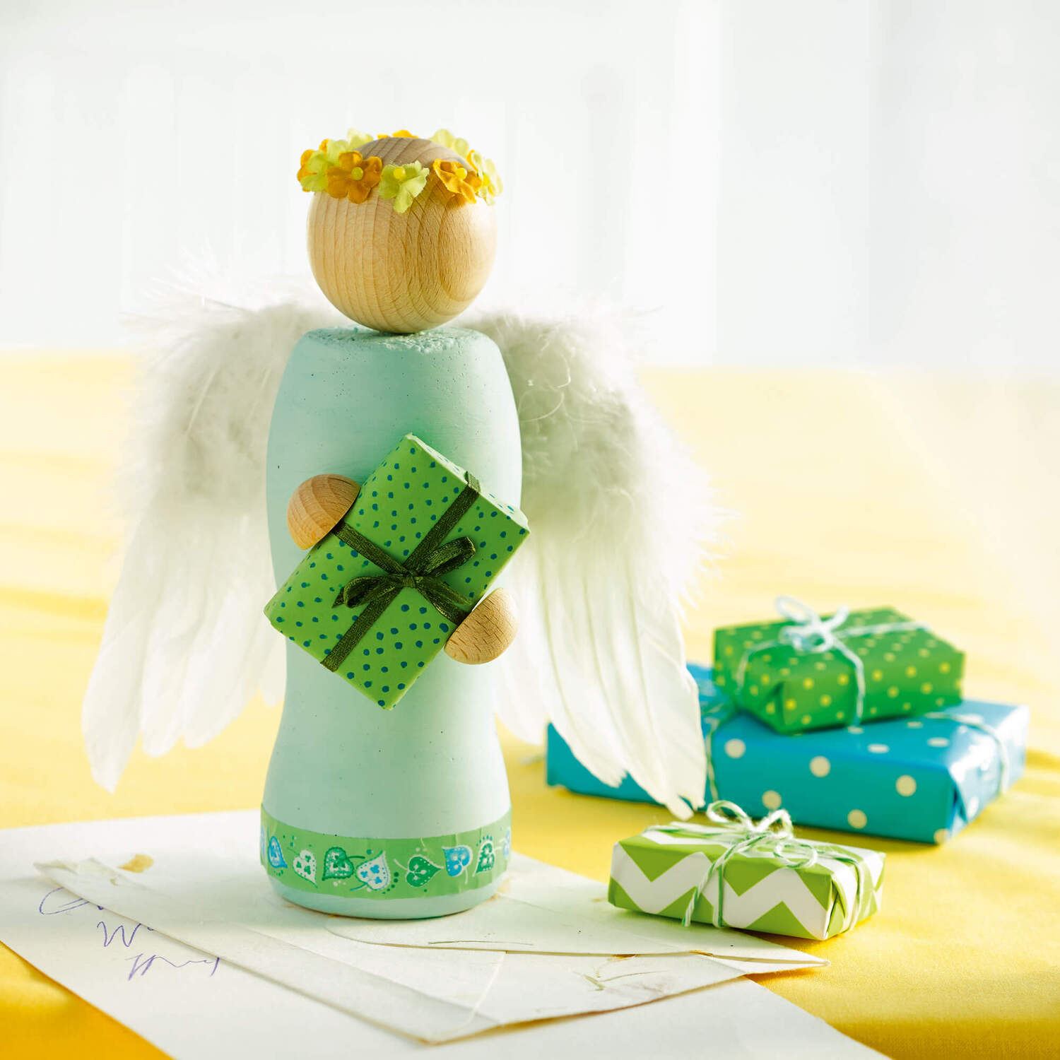 Bastelanleitung Engel aus Beton: Ein Engel mit Flügeln hält ein Geschenk, umgeben von weiteren Geschenken auf einem Tisch.