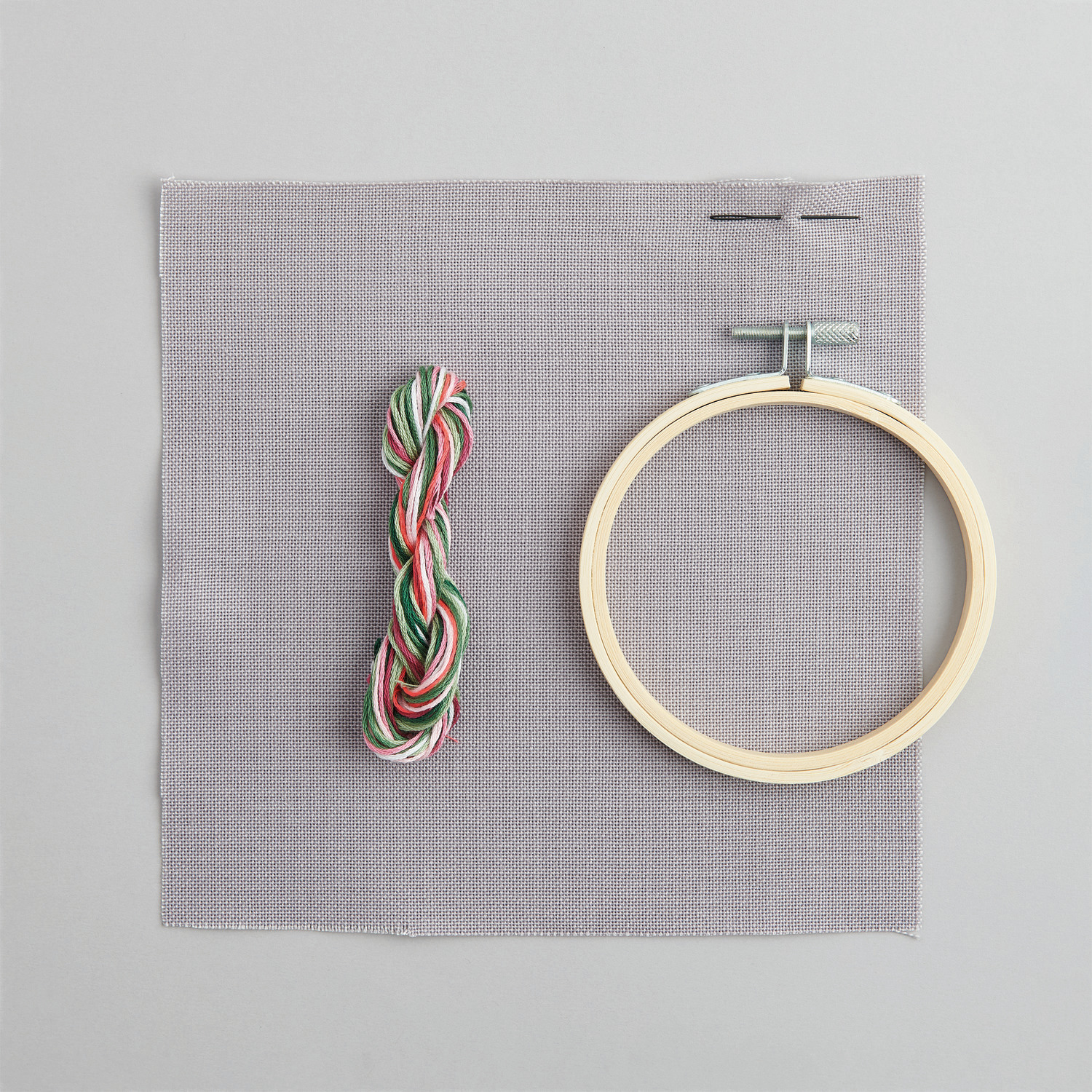 Stickpackung Bild Blumenkranz: Grauer Stoff, bunte Fäden, Holzrahmen Ø10cm, ideal für kreative Stickprojekte.