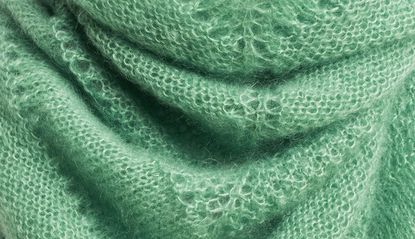 Strickanleitung Dreieckstuch mit Lochmuster in zartem Grün, zeigt feine Details und weiche Textur des gestrickten Materials.