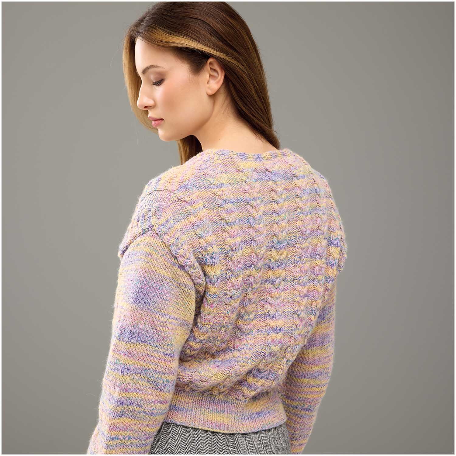 Strickset Jacke Modell 06: Frau trägt pastellfarbene Strickjacke mit Zopfmuster, Rückansicht.