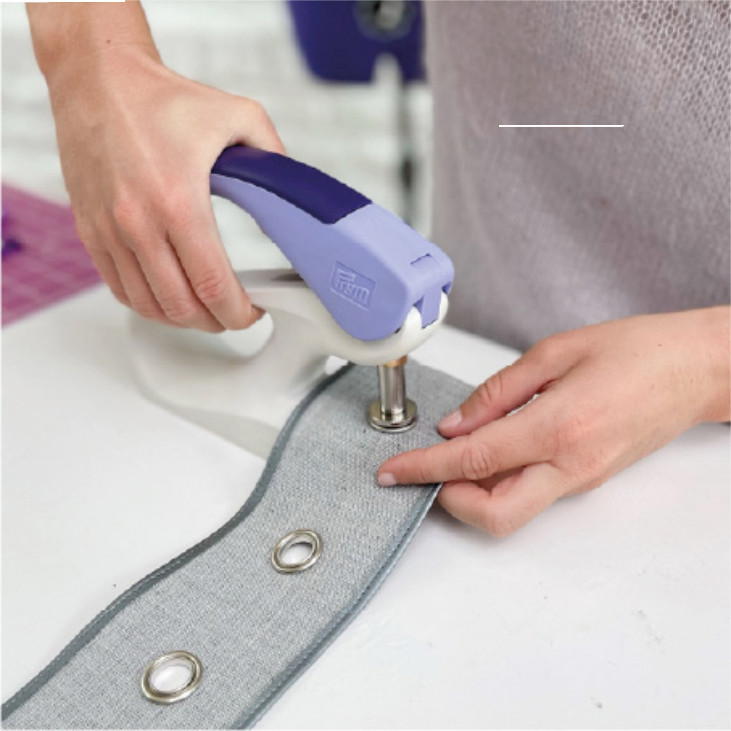 Vario Creative Tool - Stanzwerkzeug von Prym in Aktion auf grauem Stoff mit Ösen.