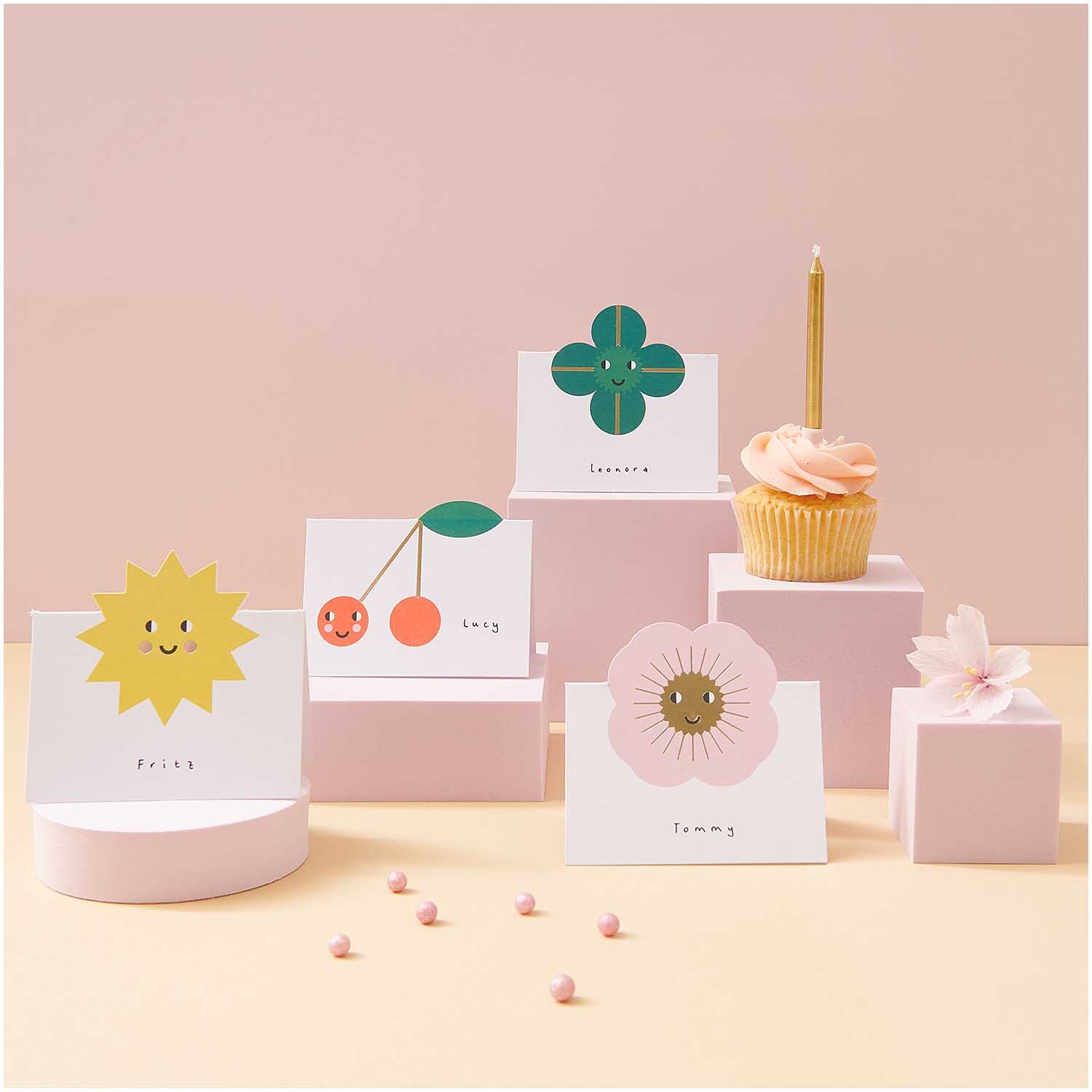 Paper Poetry Tischkarten Mix mit fröhlichen Motiven auf rosa Podesten, ideal für Feiern.
