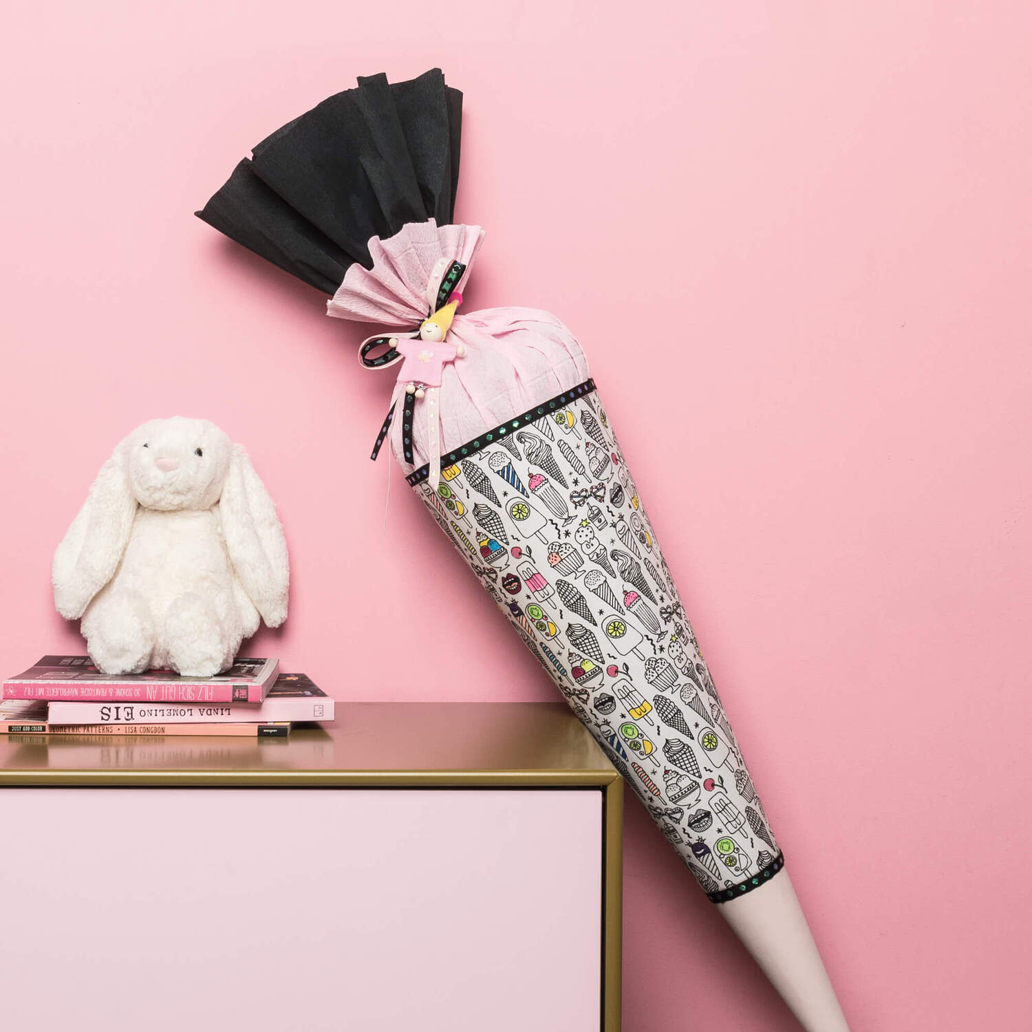 Bastelanleitung Schultüte aus Stoff: Eine bunte Schultüte mit schwarzem und rosa Stoff, dekorativ auf einem Tisch neben einem Plüschhasen platziert.