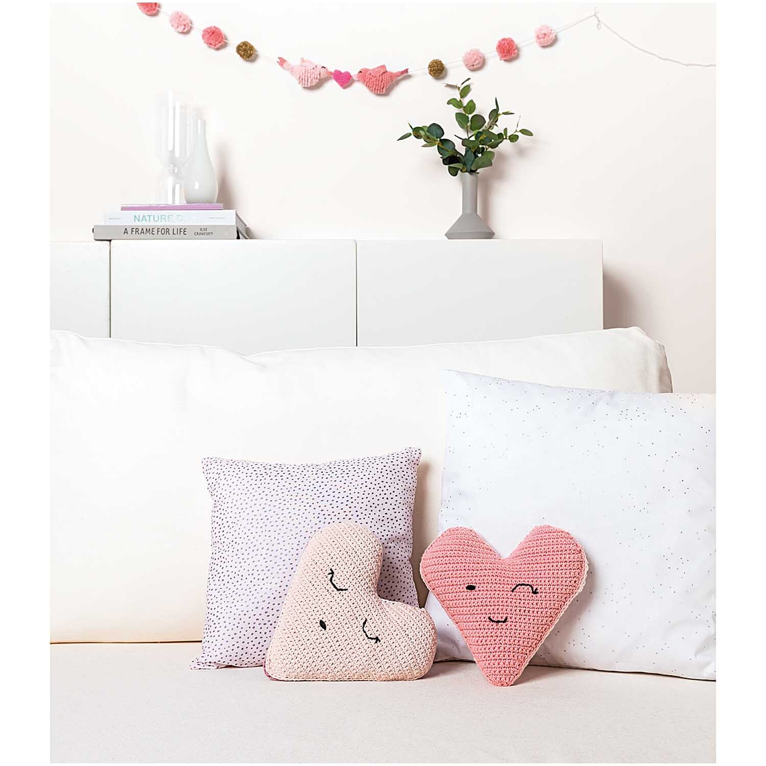 Creative Ricorumi dk: Zwei gehäkelte Herz-Kissen in Rosa auf einem Sofa, dekoriert mit einer Girlande.
