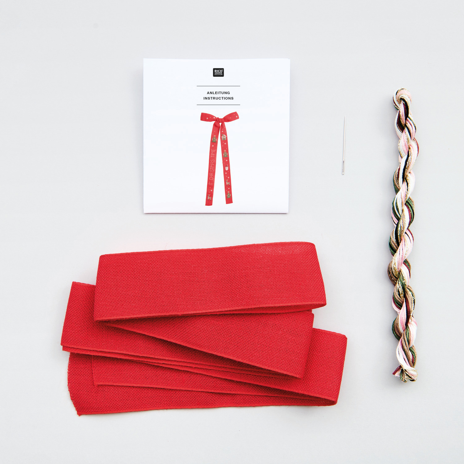 Stickpackung Schleife It's Christmas Time, Rico Design. Rotes Band, Stickgarn und Nadel auf hellem Hintergrund. Perfekt für festliche Dekorationen.
