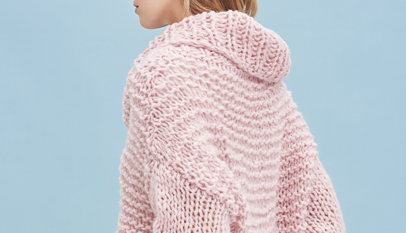 Strickanleitung Pullover aus Mohair Soft: Rosa gestrickter Pullover mit Kapuze vor blauem Hintergrund.