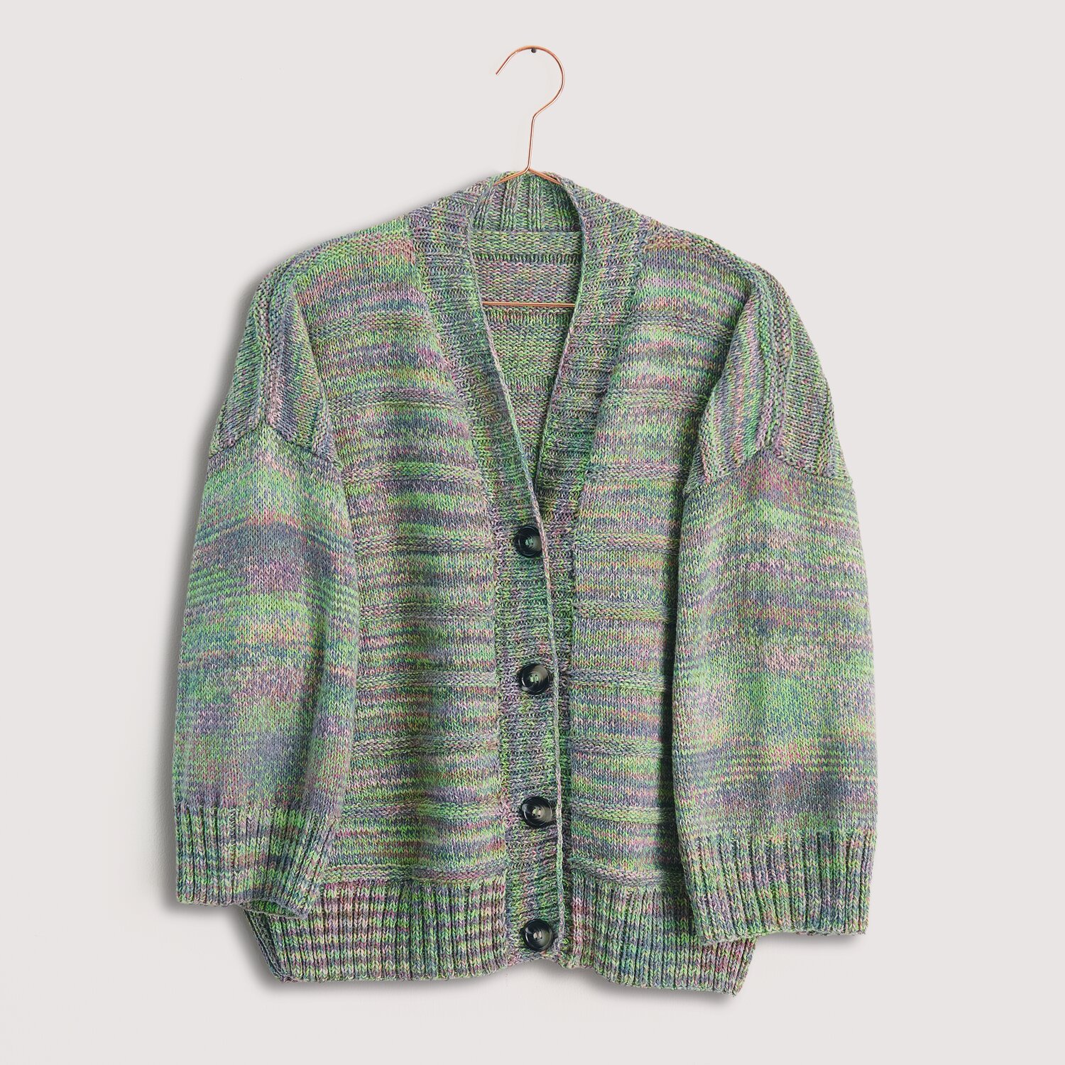 Strickset Jacke Modell 19 aus Die Neue Masche No. 12, gestrickt in grünen und lila Tönen, präsentiert auf einem Kleiderbügel.