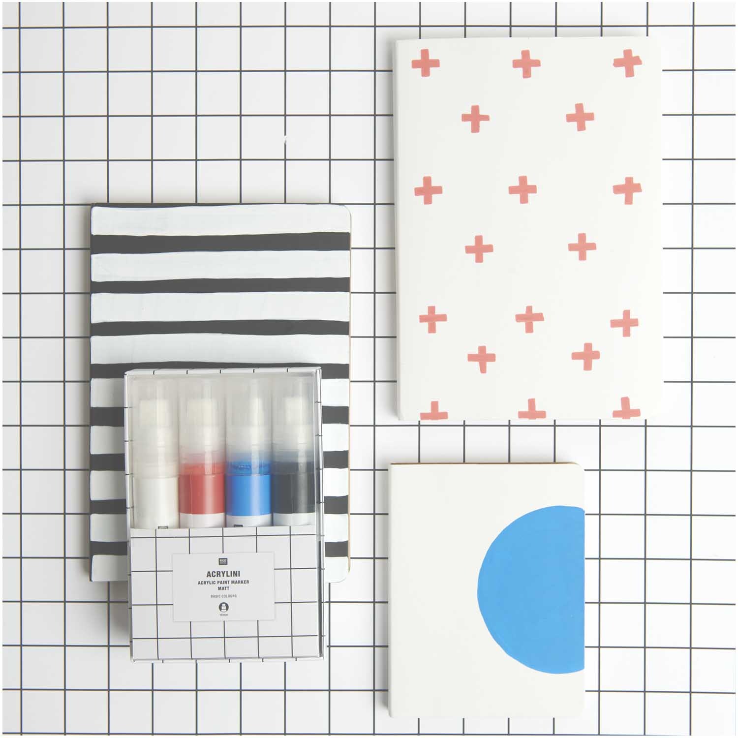 Acrylini Marker Set XL Basic, 15mm 4 Farben, auf kariertem Hintergrund mit Notizbüchern.