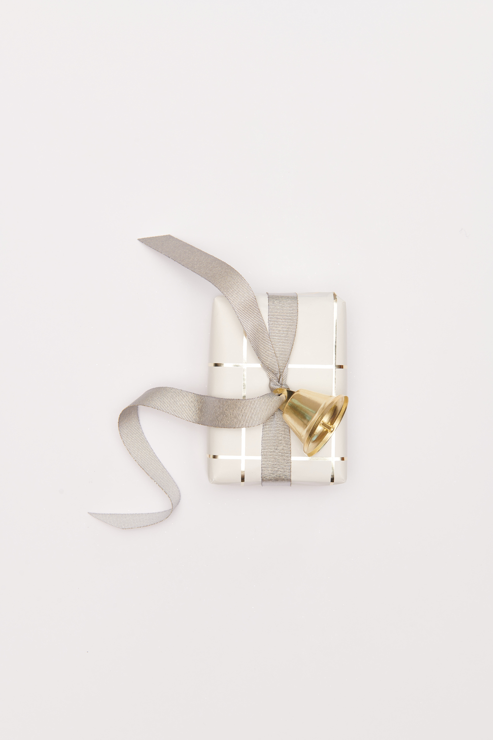 Metallglöckchen goldfarbig von Rico Design, dekoriert auf einem Geschenk mit grauem Band.