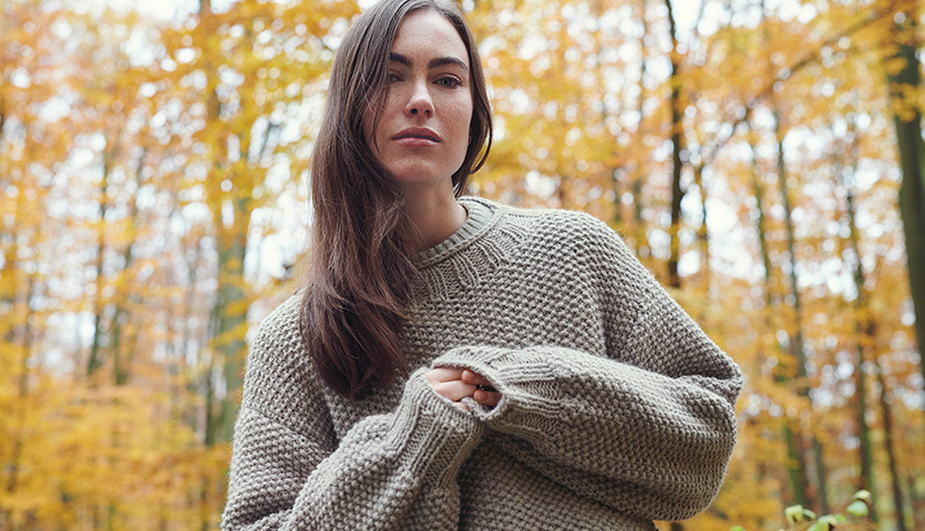 Strickanleitung Pullover und Streifenmütze aus Essentials Alpaca Twist chunky: Frau im beigen Strickpullover im herbstlichen Wald.