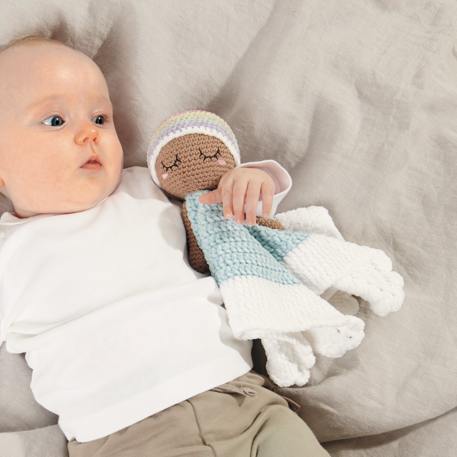 Ricorumi Baby Blankies Nilli Nilli: Ein Baby hält eine gehäkelte Puppe in Pastellfarben von Rico Design.