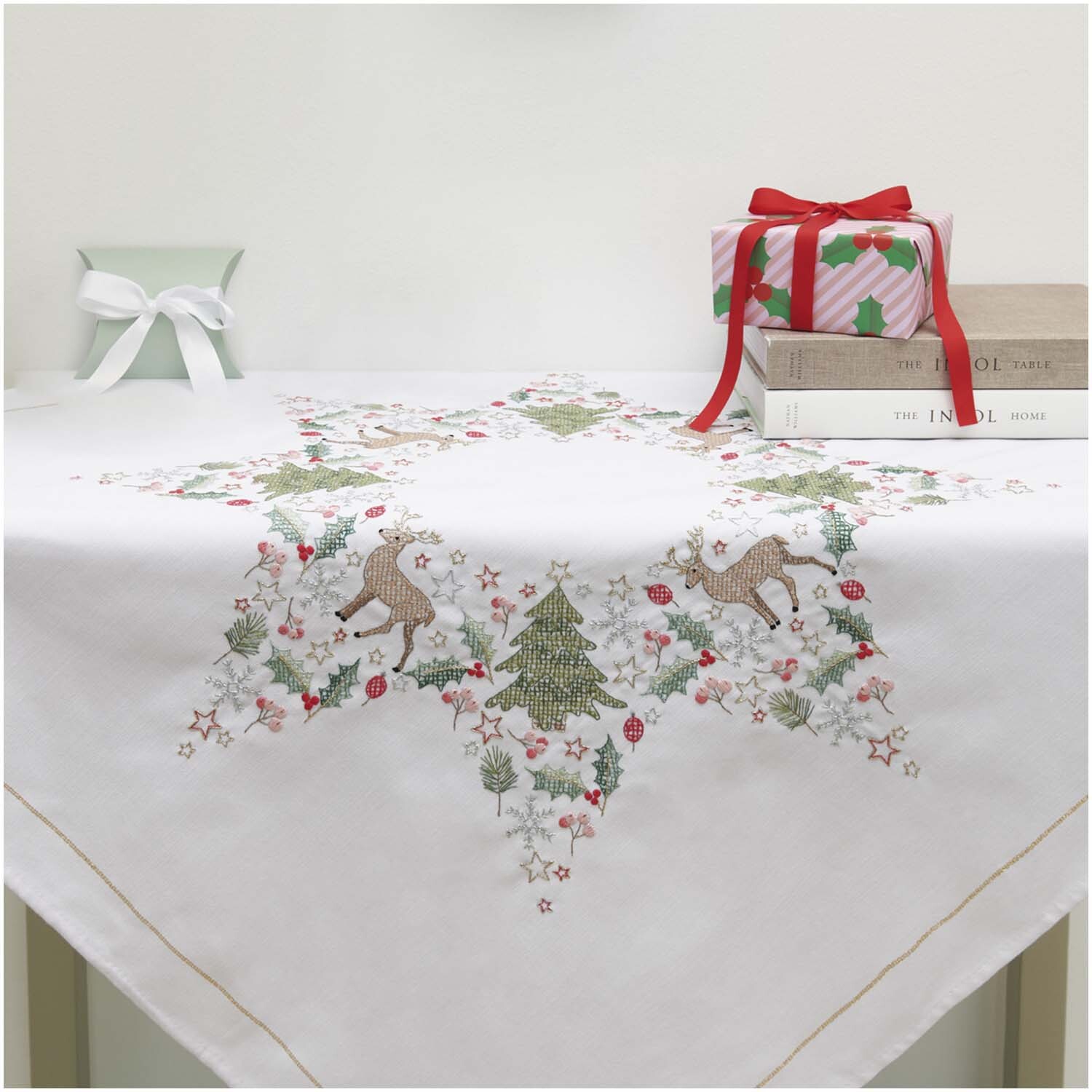Stickpackung Tischdecke Sternenkranz 90x90cm mit weihnachtlichem Motiv aus Rentieren und Tannenbäumen, dekoriert auf einem Tisch.