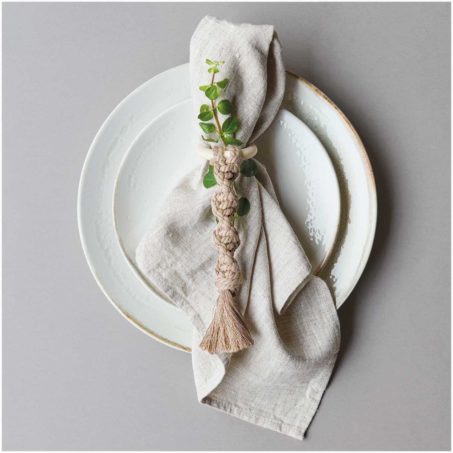 Creative Cotton Cord Makramee-Garn von Rico Design in Creme, dekorativ als Serviettenring mit Blattmotiv auf einem Teller arrangiert.