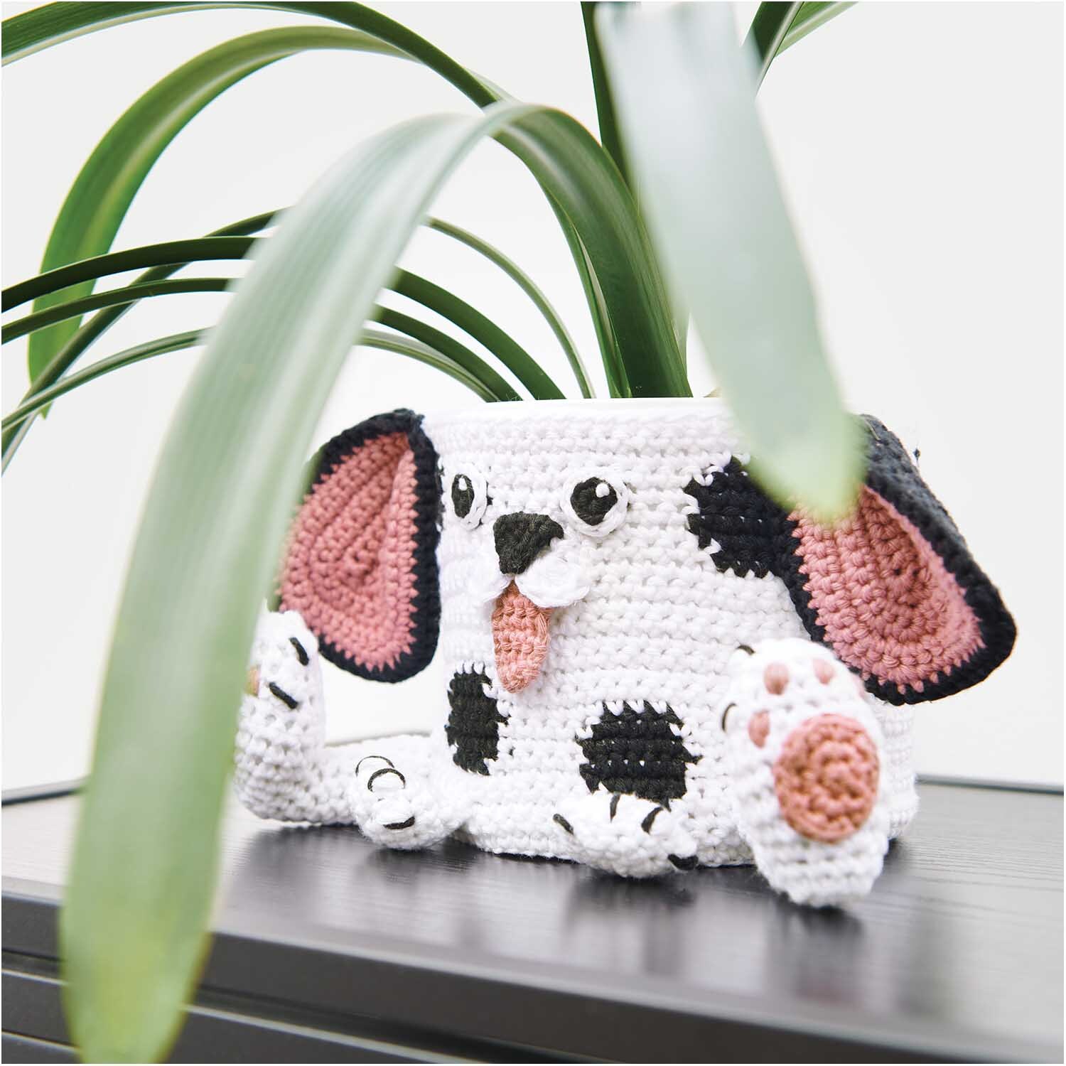 Creative Cotton aran: Gehäkelter Hundekorb mit schwarzen und weißen Details, dekoriert mit rosa Ohren und Pfoten, von Rico Design.