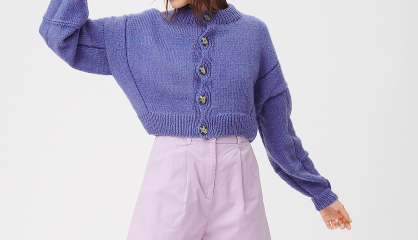 Strickanleitung Jacke aus Creative Fluffily dk: Frau trägt lila Strickjacke mit Knöpfen, kombiniert mit hellvioletter Hose.