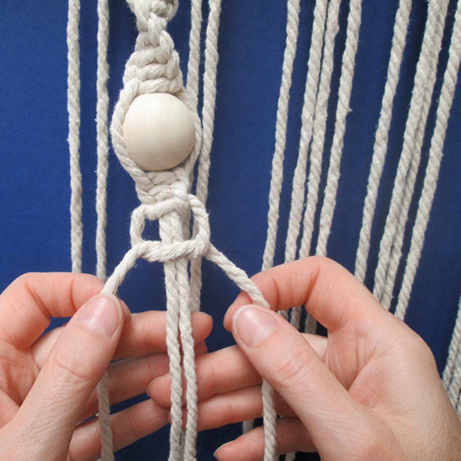 Baumwollkordel für Makramee in Creme, 5mm dick, 80m lang. Hände knoten die Kordel um eine Holzkugel. Ideal für kreative Projekte.