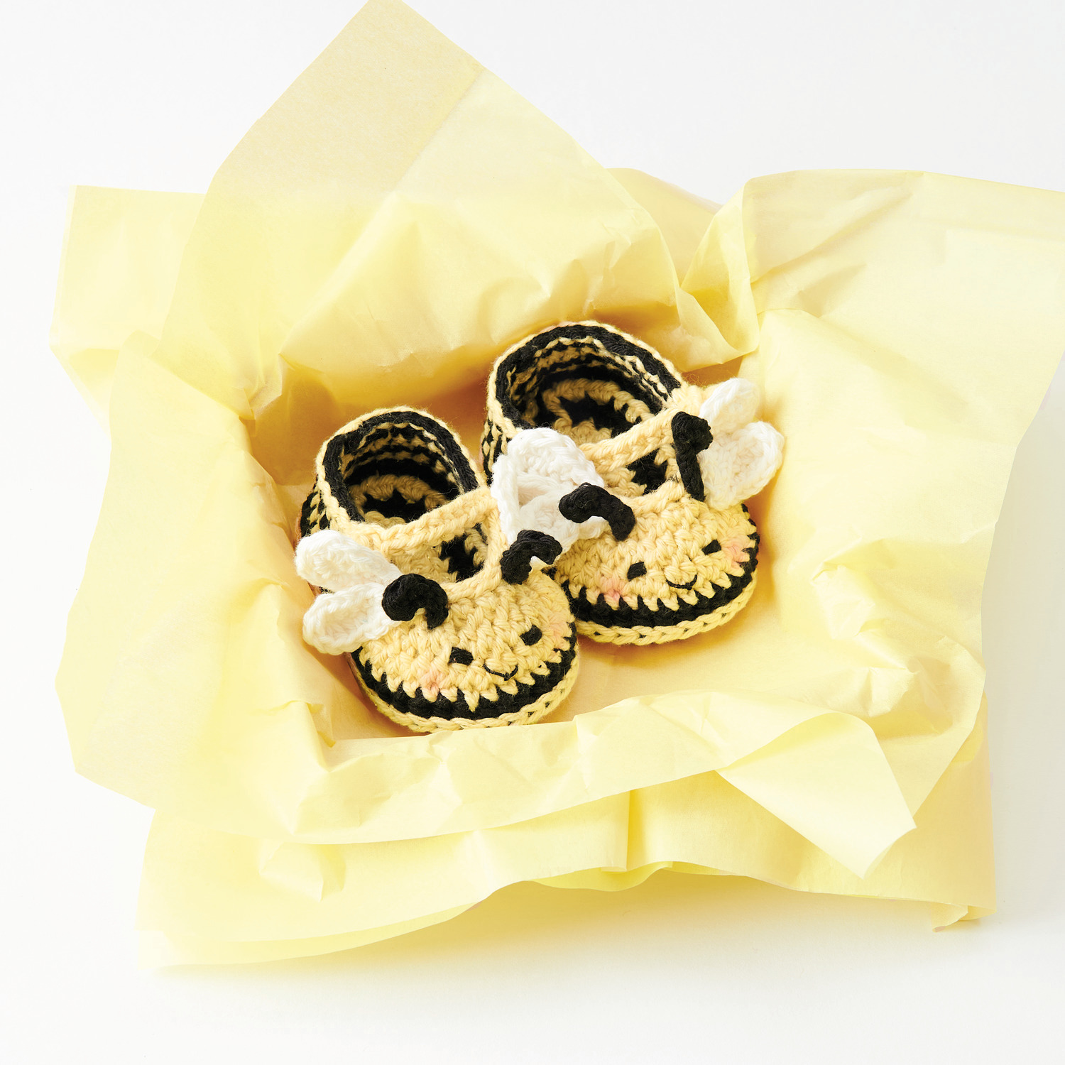 Ricorumi Häkelset Baby Booties Biene: Niedliche gehäkelte Babyschuhe in Bienenform auf gelbem Papier. Ideal für kreative Handarbeitsprojekte.