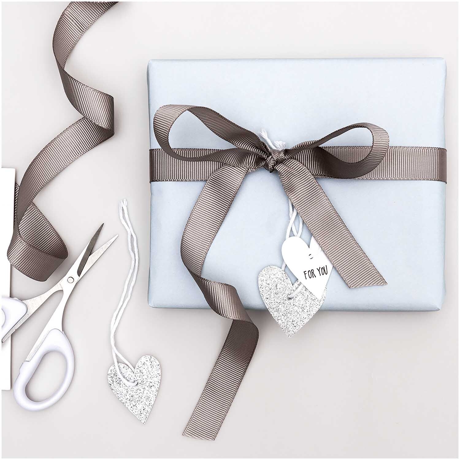 Paper Poetry Papieranhänger Herzen 3x3,5cm Glitter silber 24 Stück, dekorativ an Geschenk mit braunem Band, neben Schere und weiteren Anhängern.