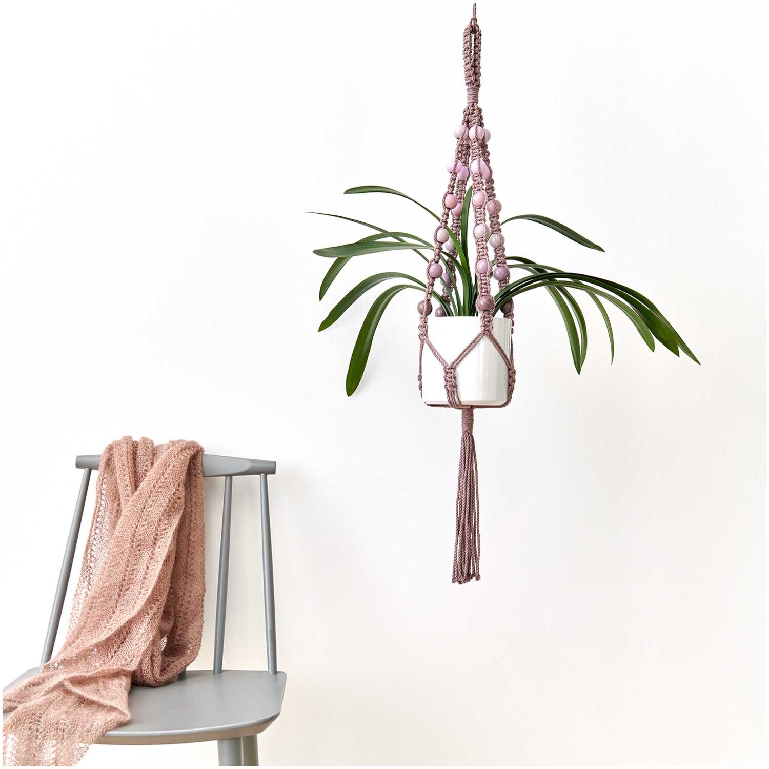 Makramee Perlen Holz Rosatöne 25mm 24 Stück: Hängender Pflanzenhalter mit rosa Holzperlen, daneben ein Stuhl mit rosa Decke.