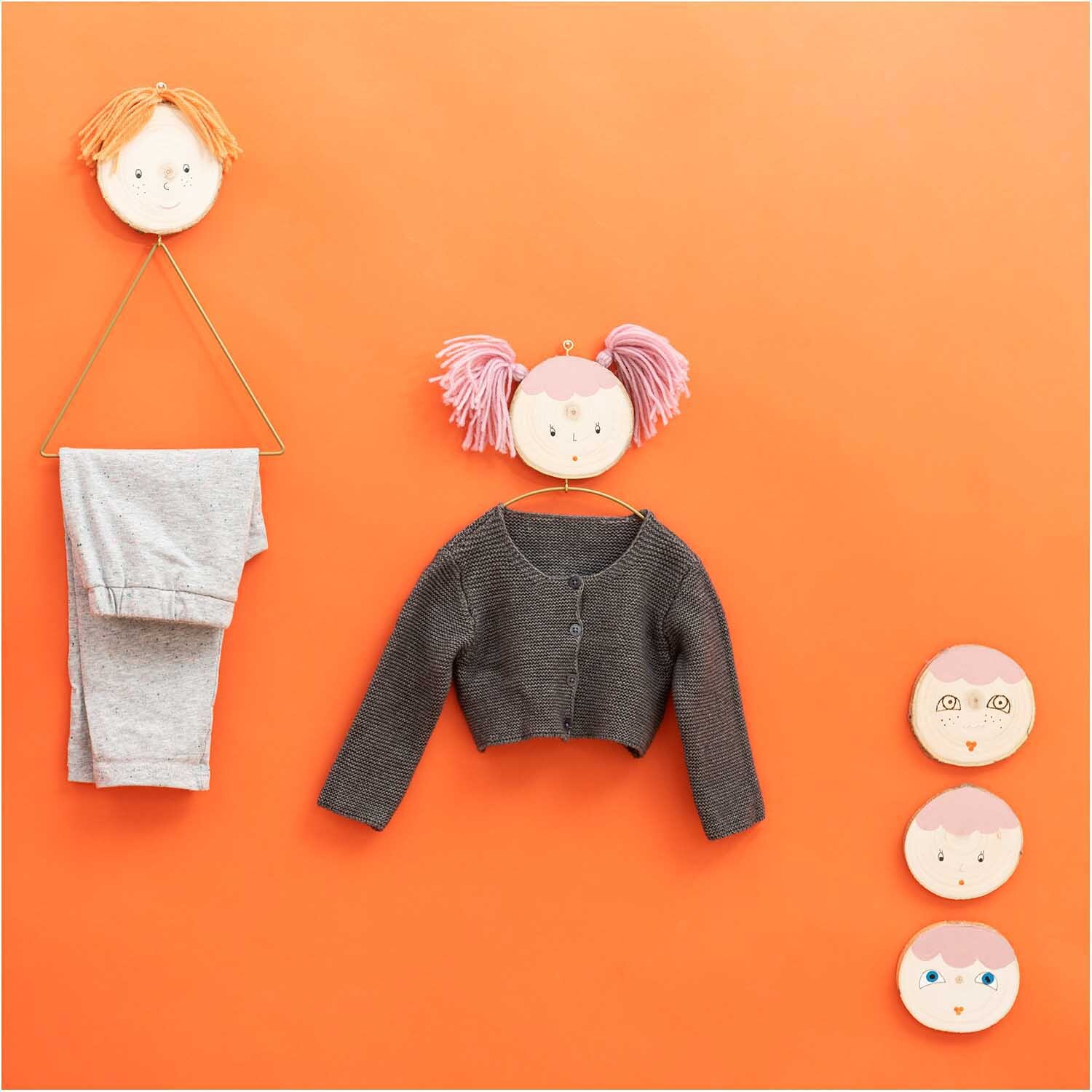 Holzscheibe groß: Dekorative Wandhaken mit Gesichtern, Kleidung und Accessoires auf orangefarbenem Hintergrund.