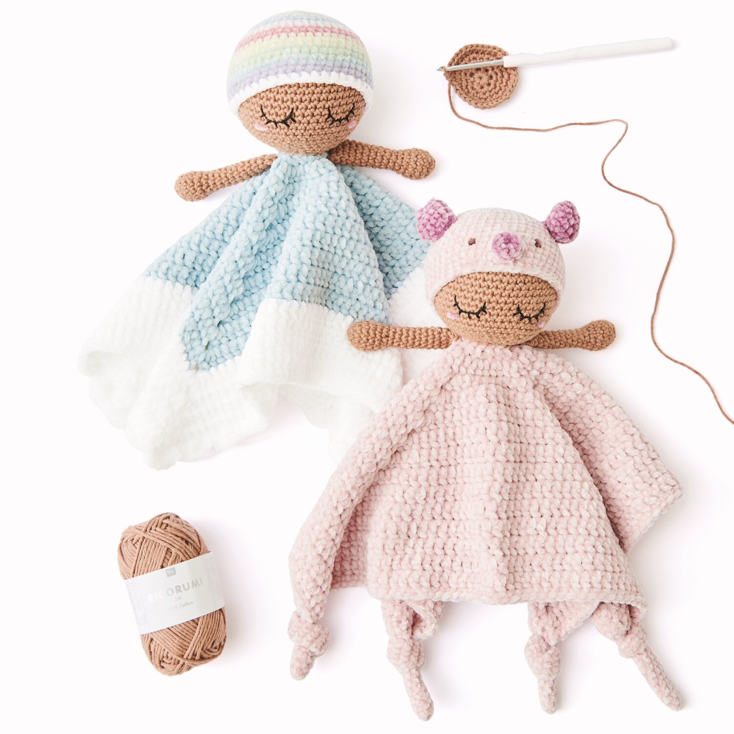 Ricorumi Baby Blankies Nilli Nilli: Zwei gehäkelte Puppen in Pastellfarben, eine in Blau-Weiß, die andere in Rosa, mit Garn und Häkelnadel.