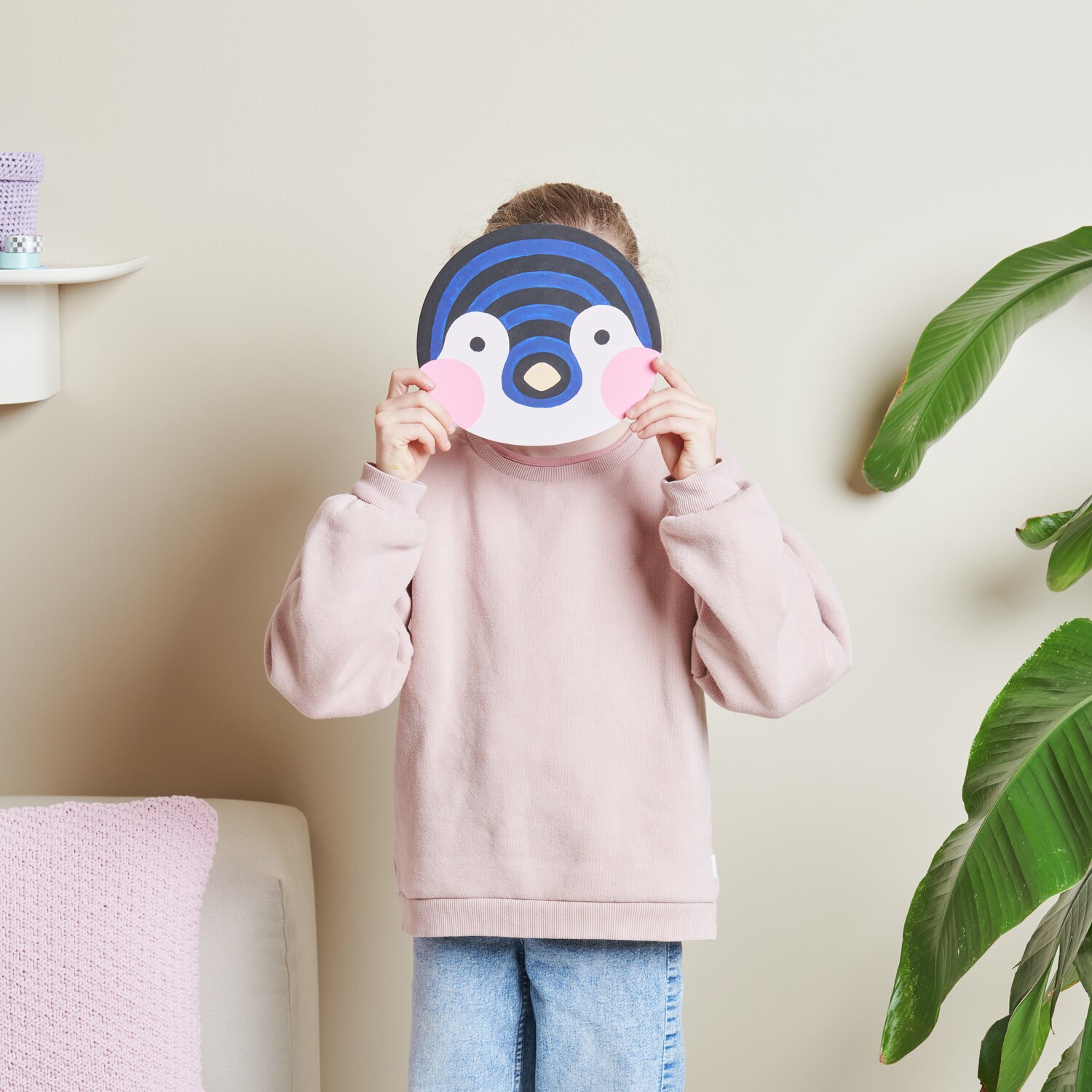 Malen nach Zahlen Pinguin von Rico Design: Kind hält Pinguin-Maske vor Gesicht, trägt rosa Pullover.