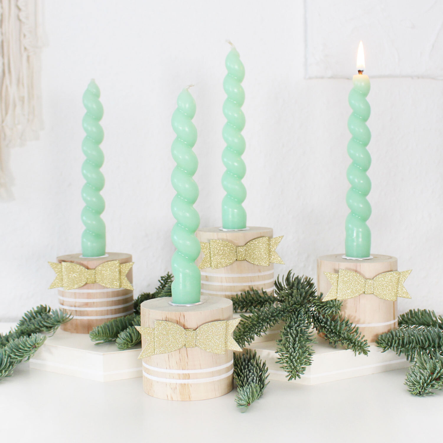 Inspiration Adventskranz mit vier mintgrünen, gedrehten Kerzen auf Holzsockeln, dekoriert mit Tannenzweigen und goldenen Schleifen.