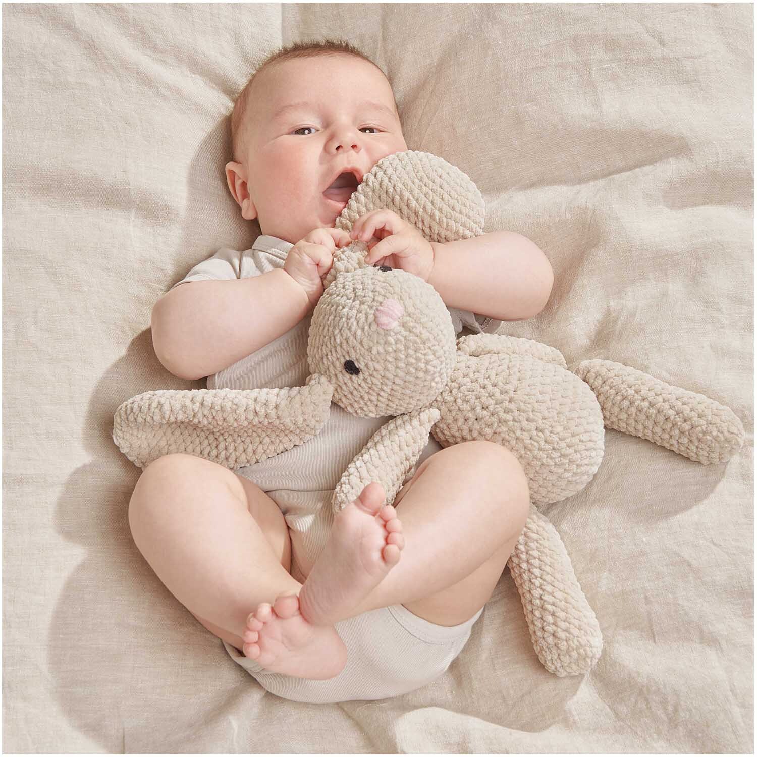 Creative Chenillove: Ein Baby kuschelt mit einem weichen, naturfarbenen Plüschhasen von Rico Design.