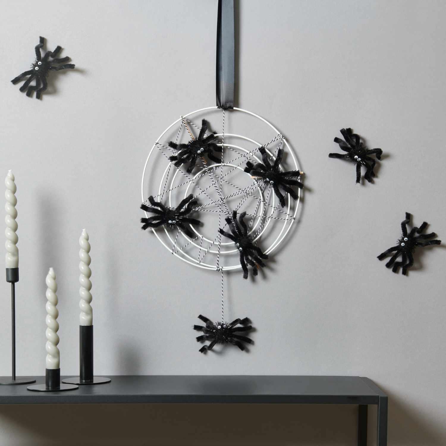 Bastelanleitung Halloween-Spinnennetz: Ein weißes Netz mit schwarzen Spinnen an einer Wand, dekoriert mit Kerzen.