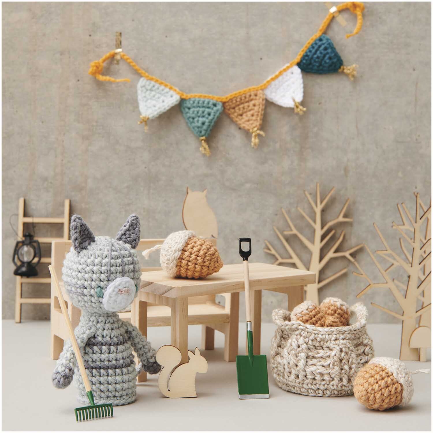 Ricorumi Set Wichtelwelt: Gehäkelte Figur mit Besen, Holztiere und bunte Girlande im Hintergrund.