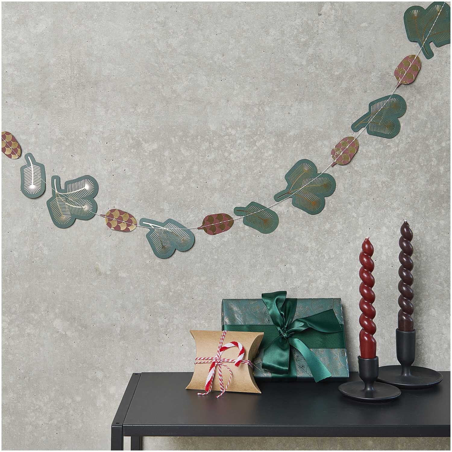 Paper Poetry genähte Girlande Zweige 2,3m von Rico Design schmückt eine Wand über einem Tisch mit Geschenken und Kerzen.