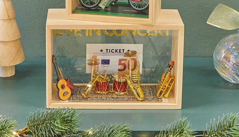Bastelanleitung Geldgeschenk für Weihnachten: Holzrahmen mit Miniaturinstrumenten und Geldschein.