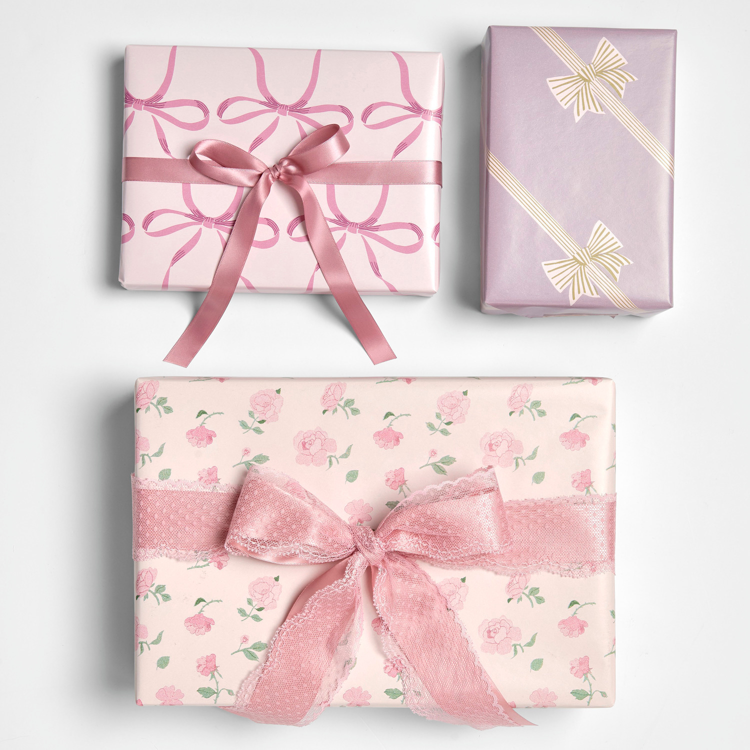 Geschenkpapier Schleifen Rosa: Drei Geschenke in rosa Papier mit Schleifen- und Rosenmuster, elegant verpackt.