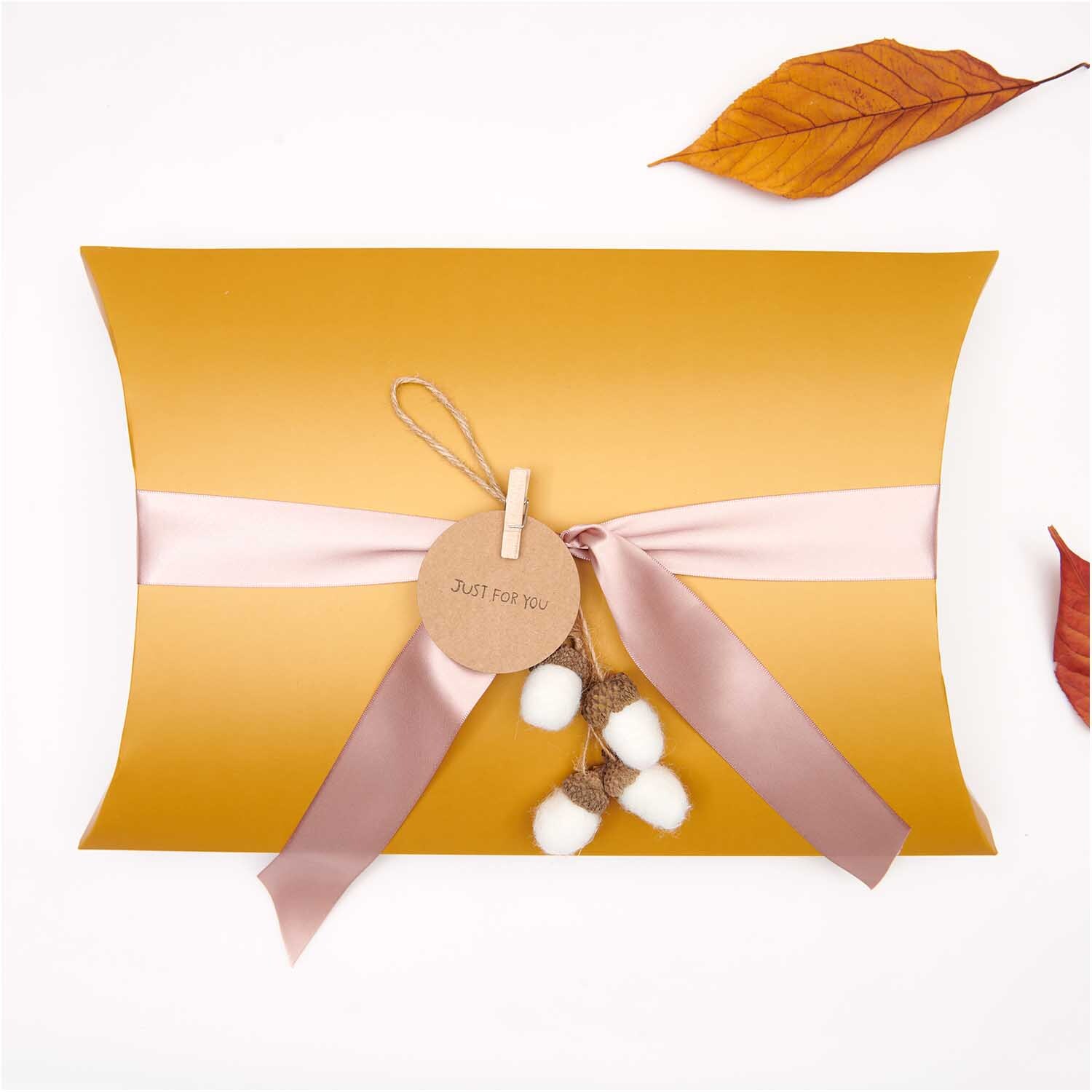 Filzhänger Eichelbündel natur 5x22cm von Rico Design, dekoriert auf einer goldenen Geschenkbox mit rosa Band und weißen Filzkugeln.