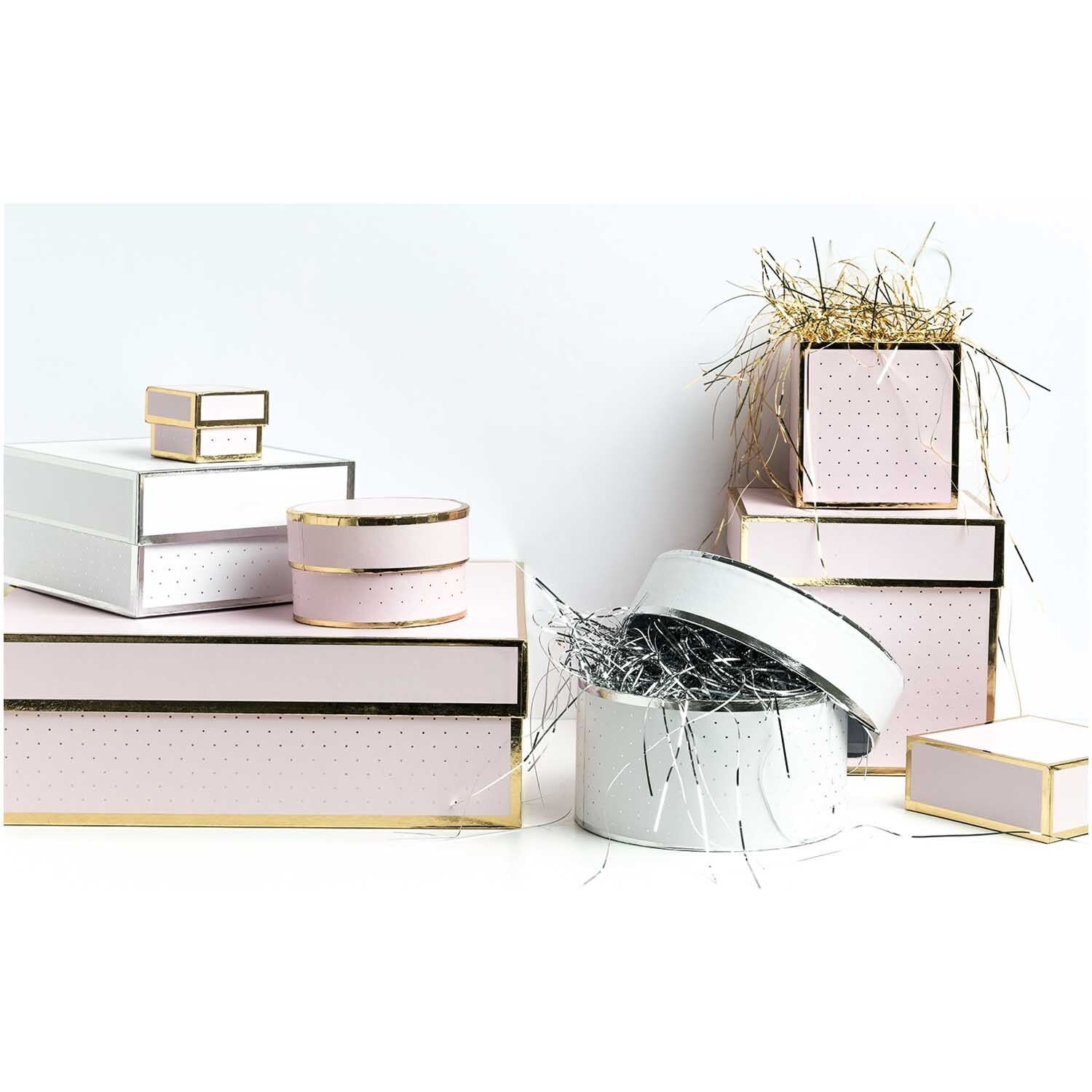 Paper Poetry Geschenkschachtel rund weiß, dekoriert mit glänzendem Füllmaterial, umgeben von eleganten, pastellfarbenen Geschenkboxen.