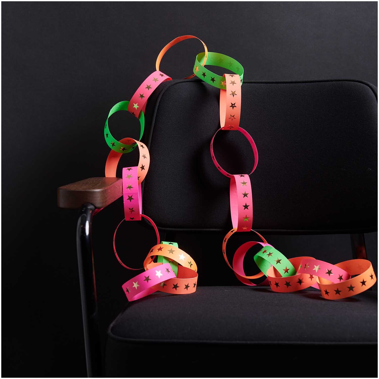 Paper Poetry Fröbelstreifen neon Sterne L 40 Stück: Bunte Papierstreifen mit Sternenmuster, dekorativ auf einem schwarzen Stuhl arrangiert.
