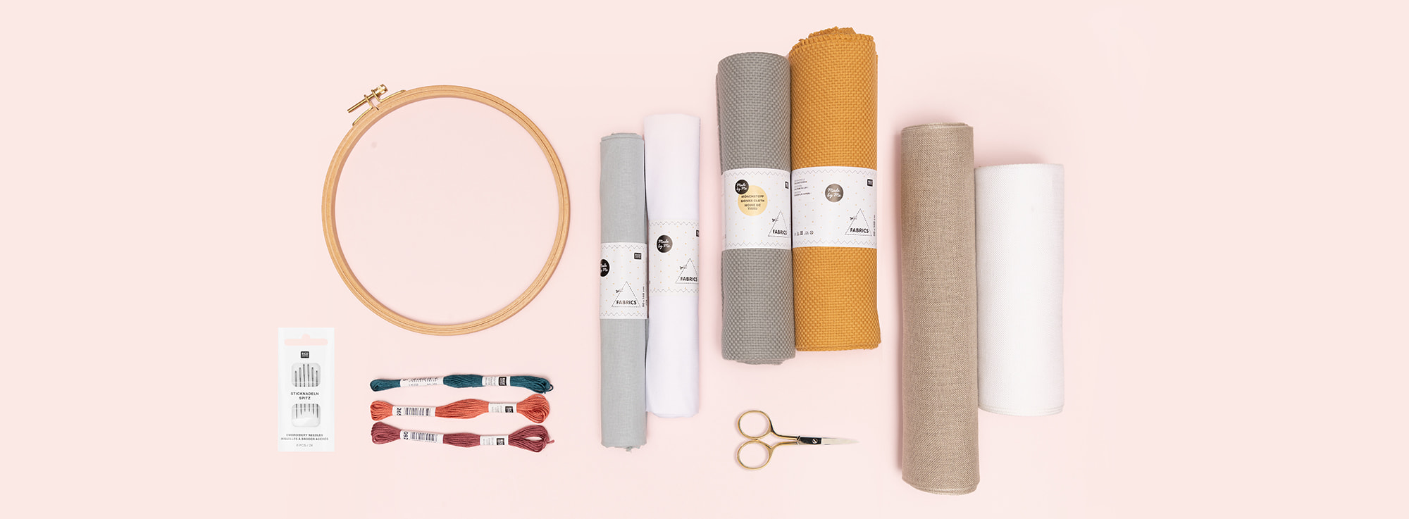Stickring, Stickgarn, Stoff und Stickzubehör liegen auf rosa Untergrund