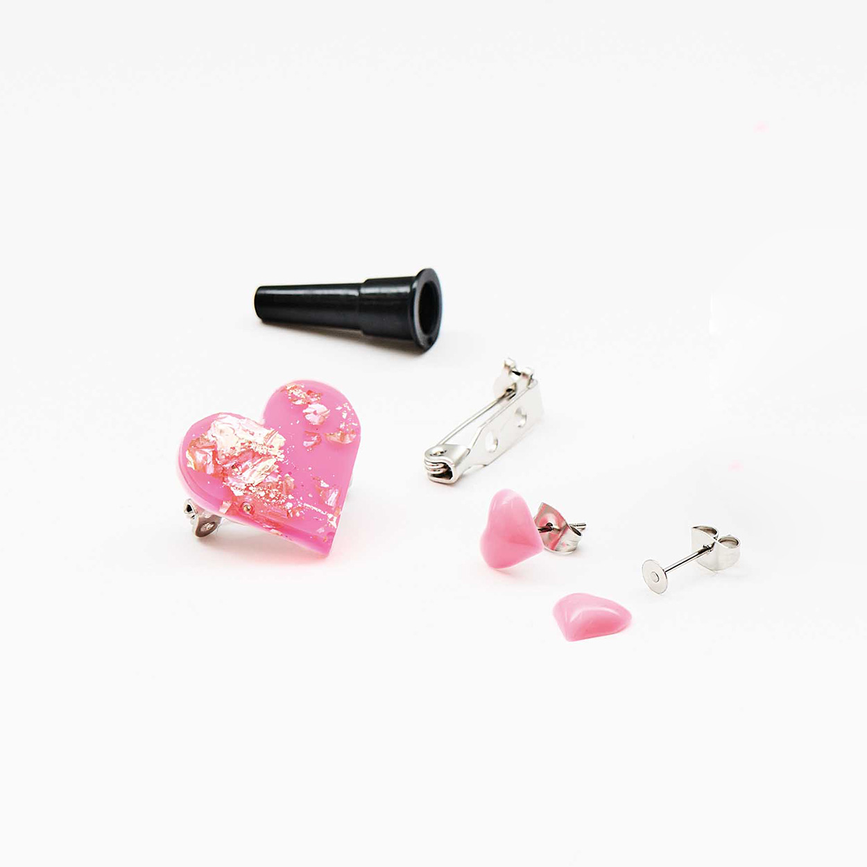 Ein pinkes Herz mit Blattgold und zwei kleinere rosa Herzen aus Resin, daneben eine Broschen-Klammer und zwei Ohrstecker.