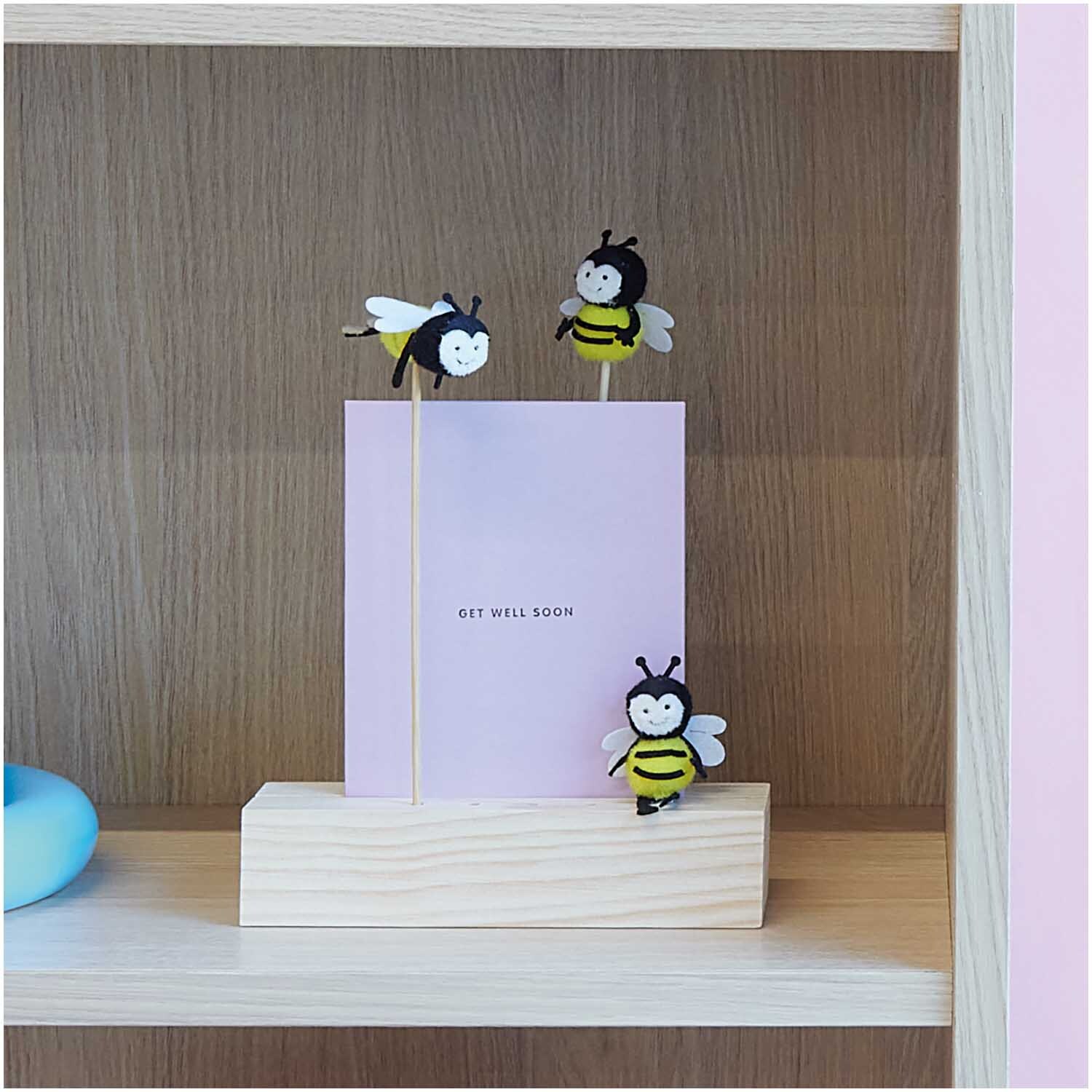 Deko-Stecker fliegende Biene 23cm von Rico Design: Drei Bienen-Stecker auf Holzsockel mit rosa Karte.