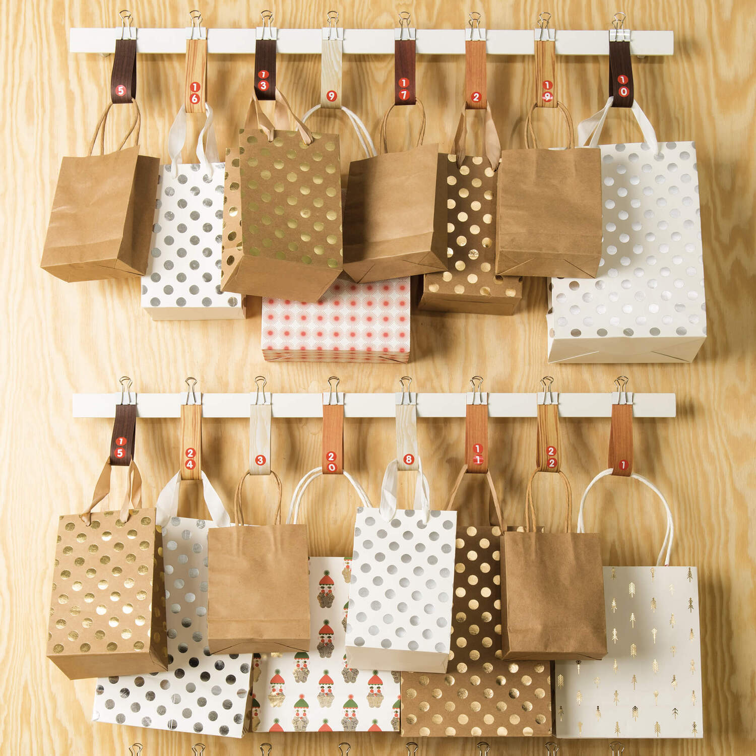 Bastelanleitung Adventskalender aus Papiertüten: Verschiedene Papiertüten in Braun und Weiß mit Mustern, aufgehängt an einer Holzleiste.
