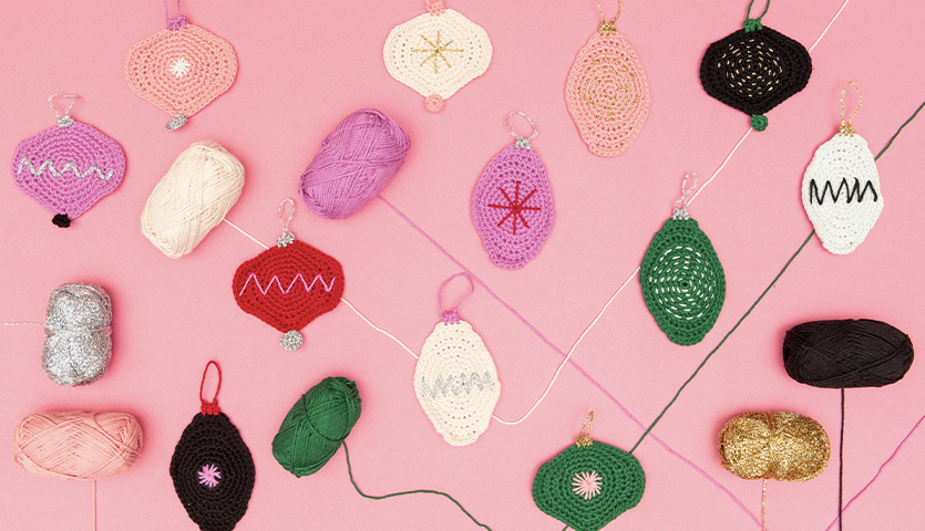 Häkelanleitung Ricorumi Christmas-Anhänger: Bunte, gehäkelte Weihnachtsanhänger und Garn auf rosa Hintergrund.