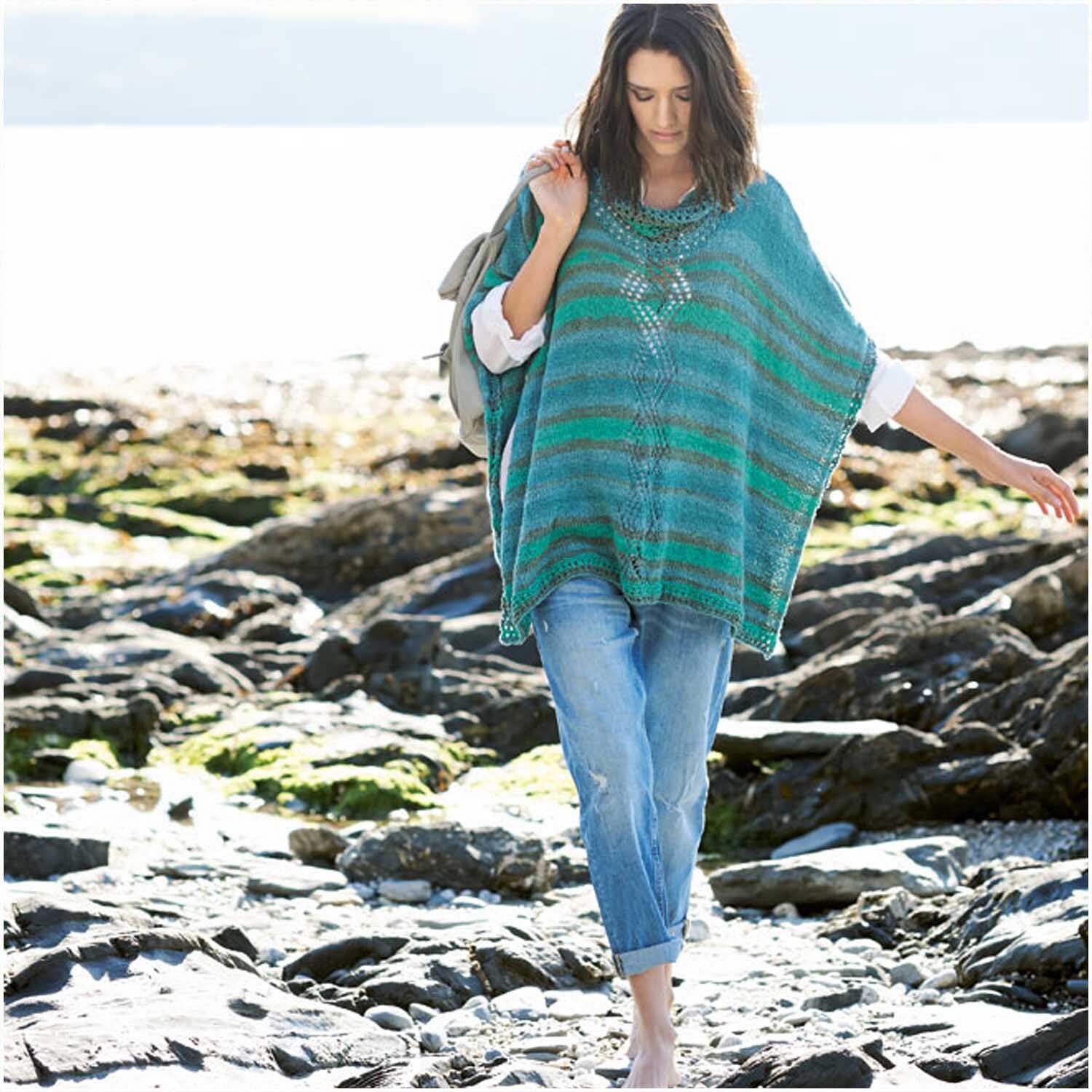 Creative Cotton Zickzack: Frau in türkisfarbenem Poncho von Rico Design am felsigen Strand.