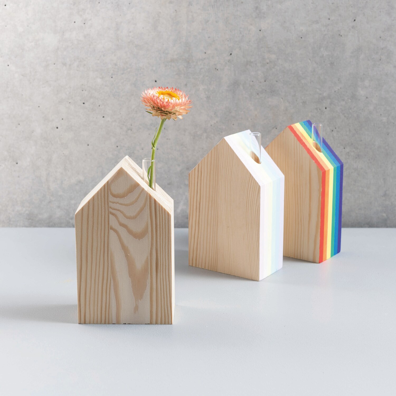 Holz-Haus mit kleiner Glasvase 9x15x5cm: Drei dekorative Holzhäuser, eines mit Blume, auf grauem Hintergrund.
