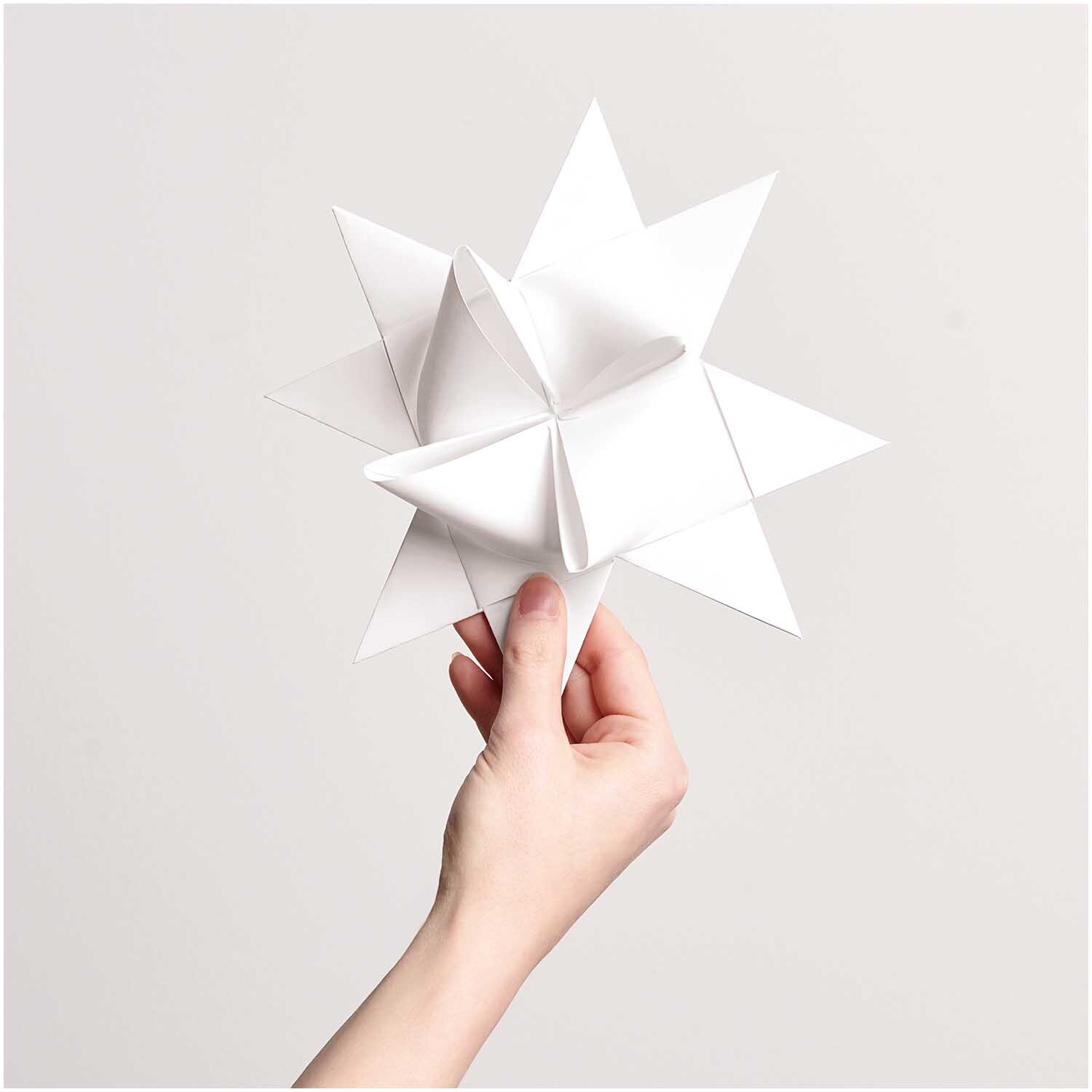 Paper Poetry Fröbelstreifen XXL in Weiß, gefaltet zu einem dekorativen Stern, gehalten von einer Hand. Ideal für kreative Bastelprojekte.